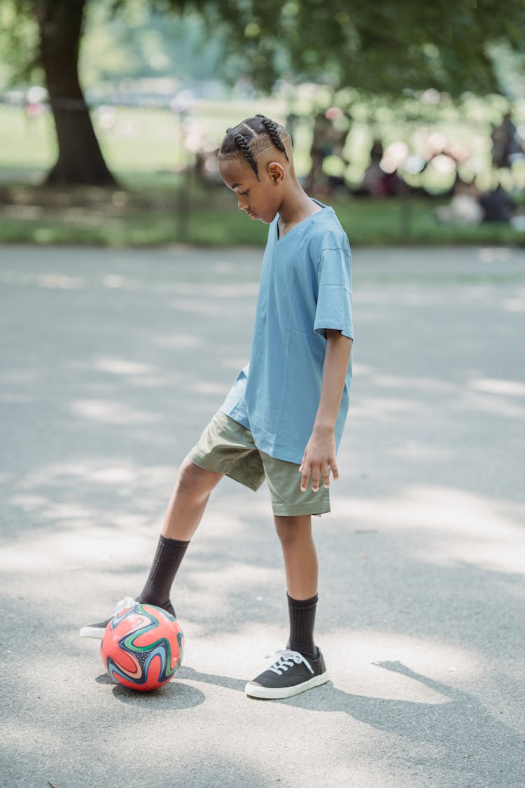 Boy Playing Football On Asphalt In A Park