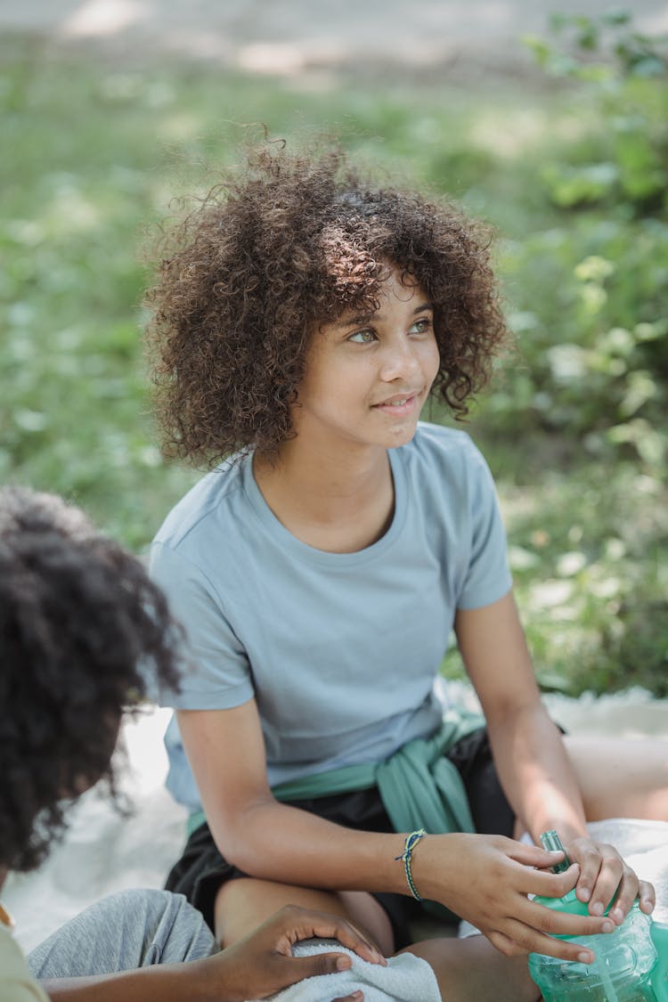 Lovely Teenage Girl With Curly Hair Sitting With Friend In Park 