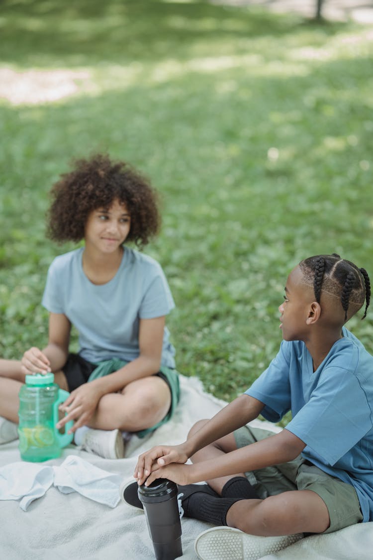 Two Kids Sitting On Blanket In Park