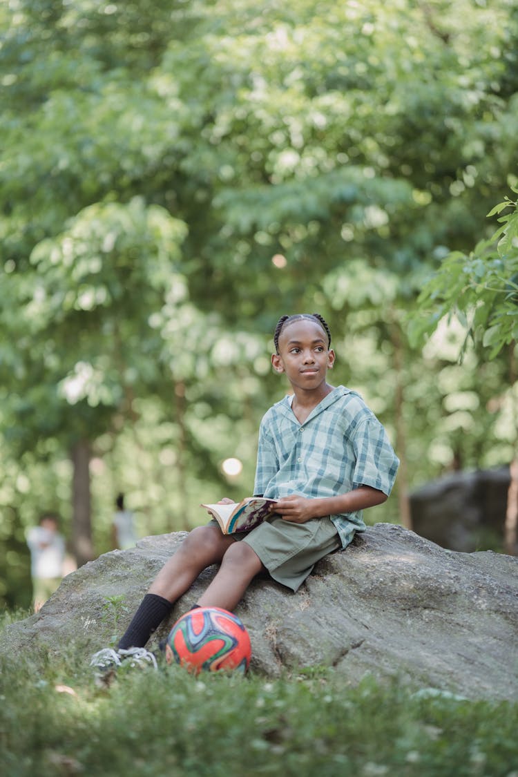 Boy Sitting With Ball On Rock