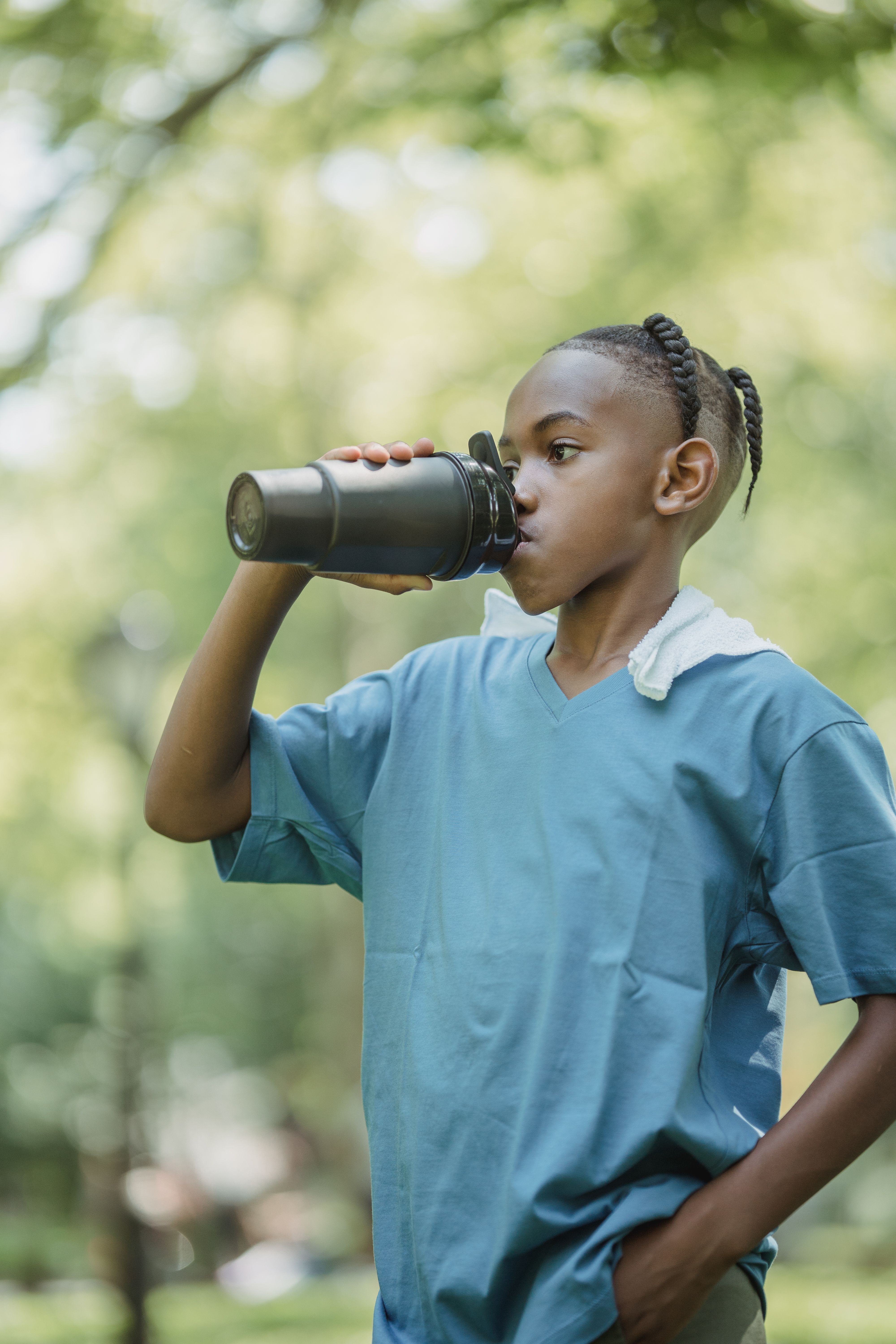 A teenage boy quenches his thirst with a water bottle in a sunny park setting.