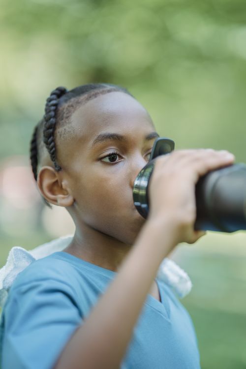 Free A young boy drinking water from a bottle in a park, staying hydrated during summer. Stock Photo