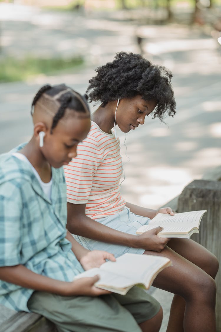 Boy And Woman With Books Sitting On Fence