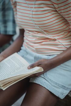Close-up of an individual reading a book, wearing casual summer attire, sitting outdoors.