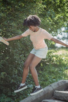 A young woman balances playfully outdoors in a vibrant summer park setting.