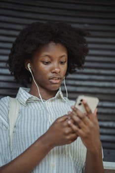 Portrait of a young African American woman using earbuds and smartphone, showcasing modern technology outdoors.