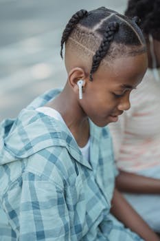 African American boy with earbuds sitting outdoors, reflecting and enjoying music.