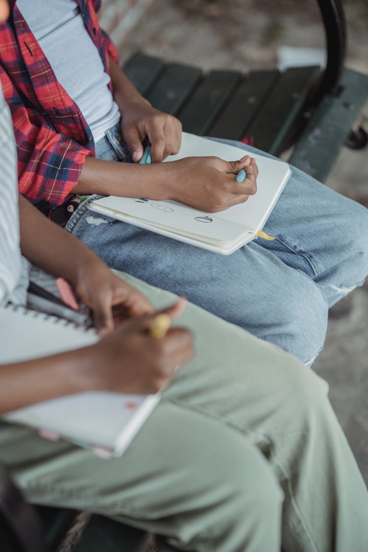 Children Sitting On Bench Drawing In Notebooks