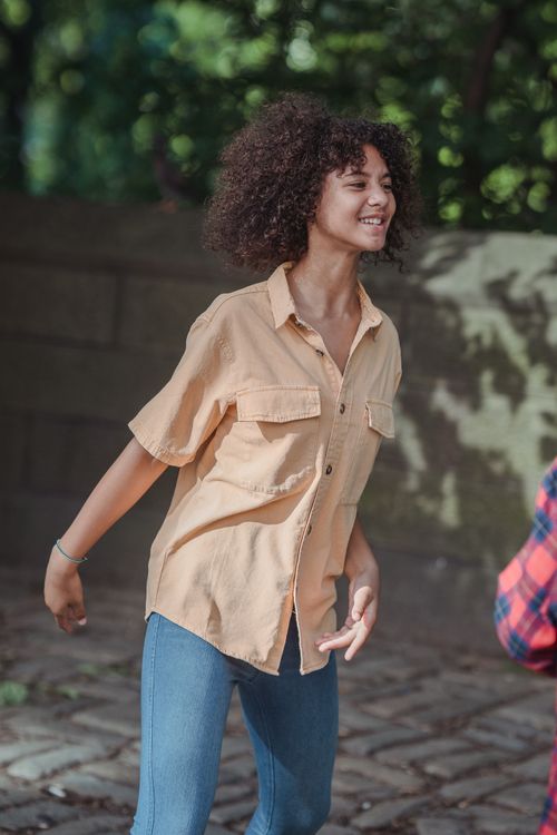 Free Young girl with curly hair smiling and enjoying a playful moment outdoors. Stock Photo