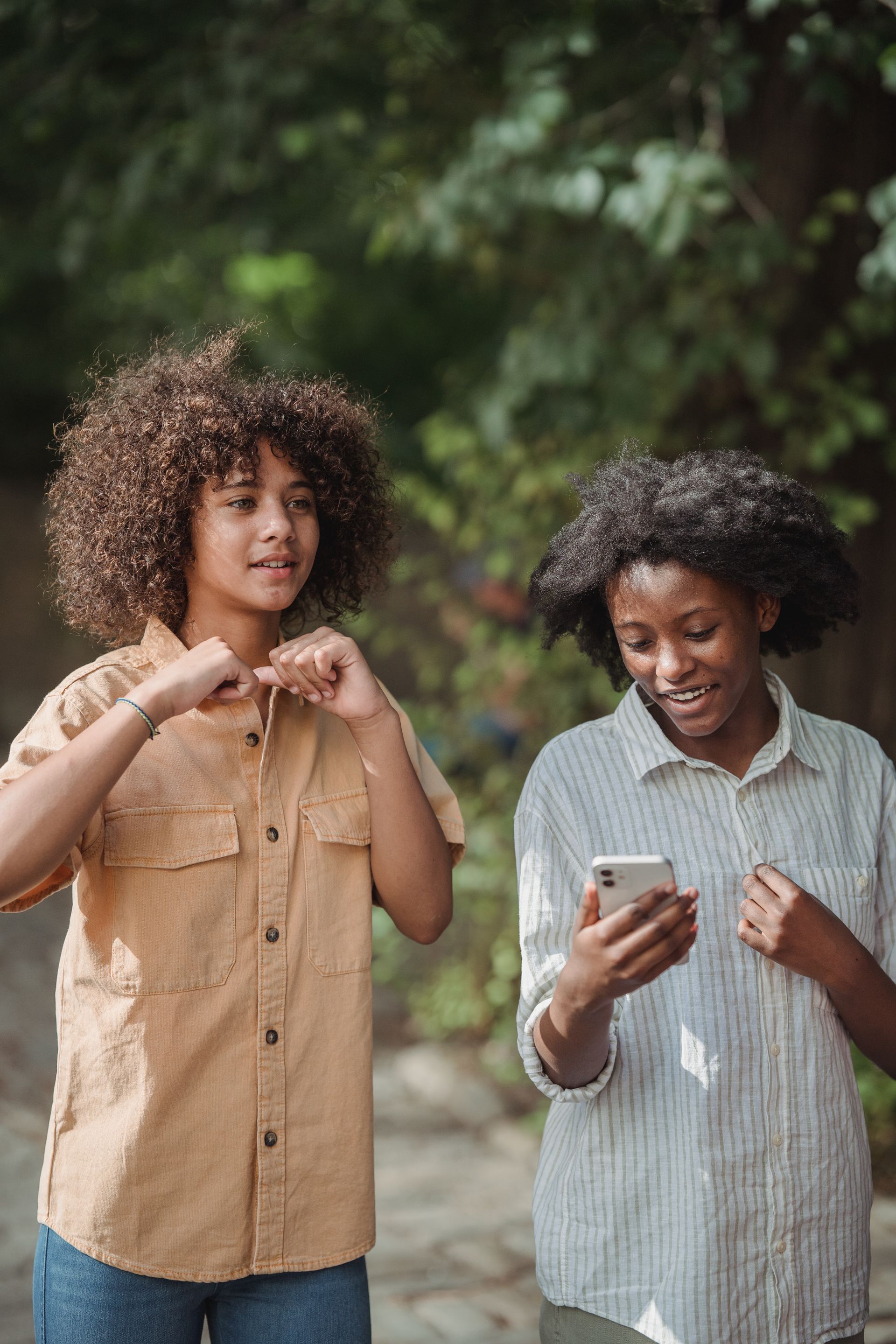 Two teenage girls smiling and looking at a smartphone together in a sunny park