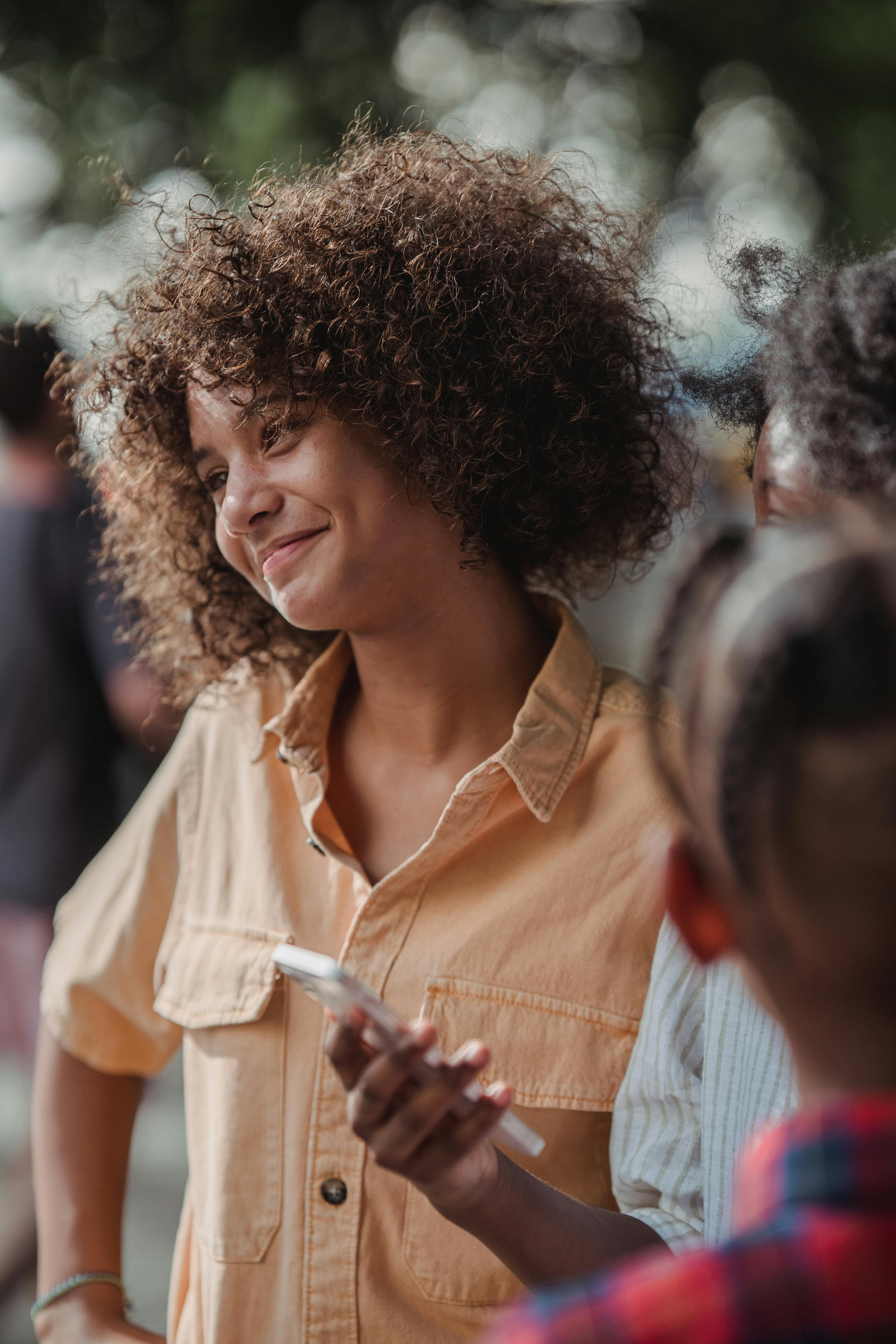 African American girl smiling with a phone, captured outdoors with a candid attitude.