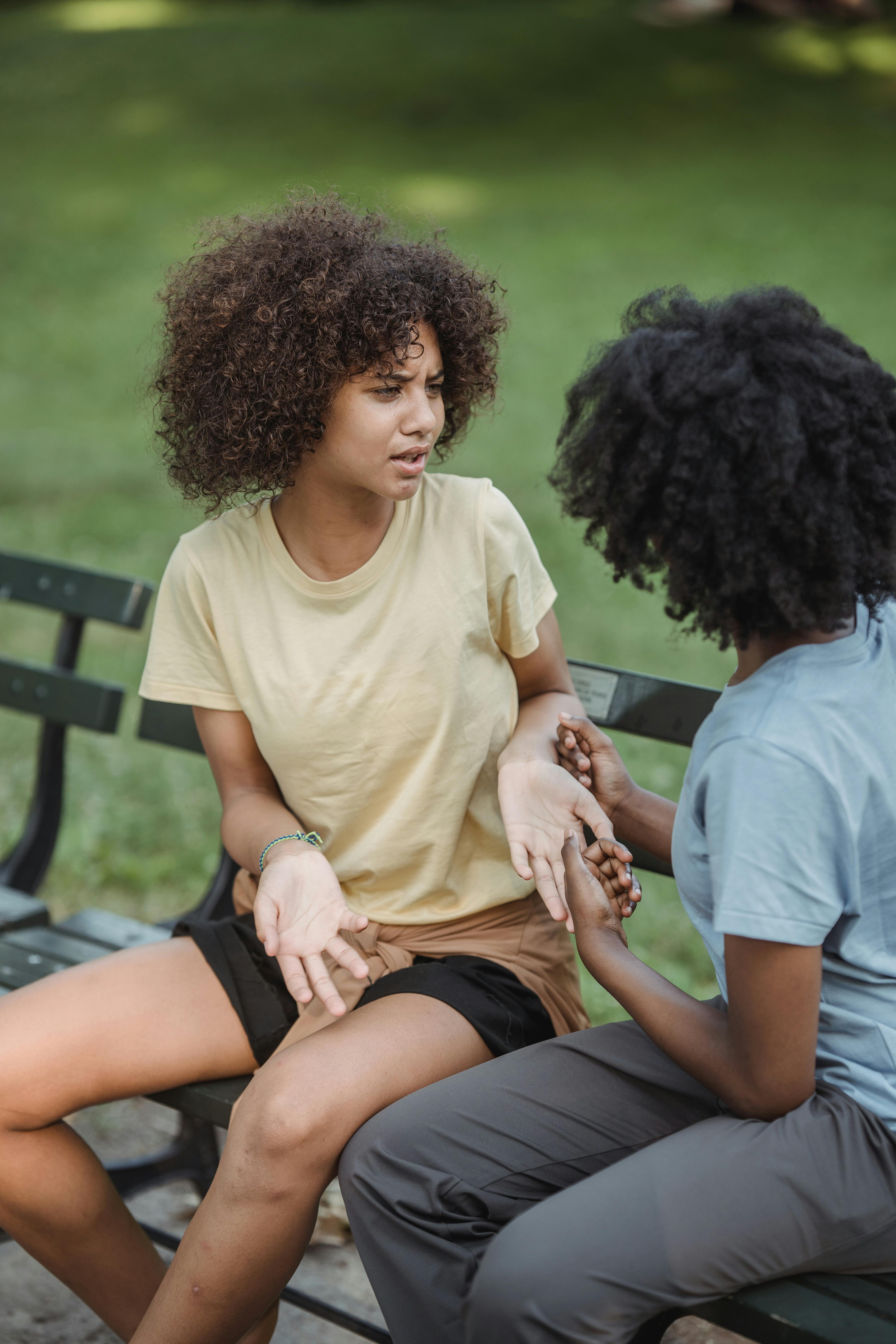 two teenage girls sitting on the bench in the park and talking