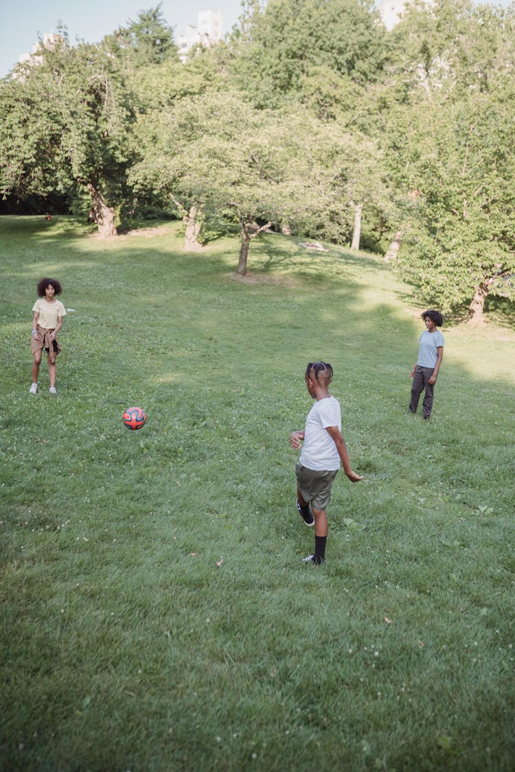 Three Kids Playing Football In The Park 
