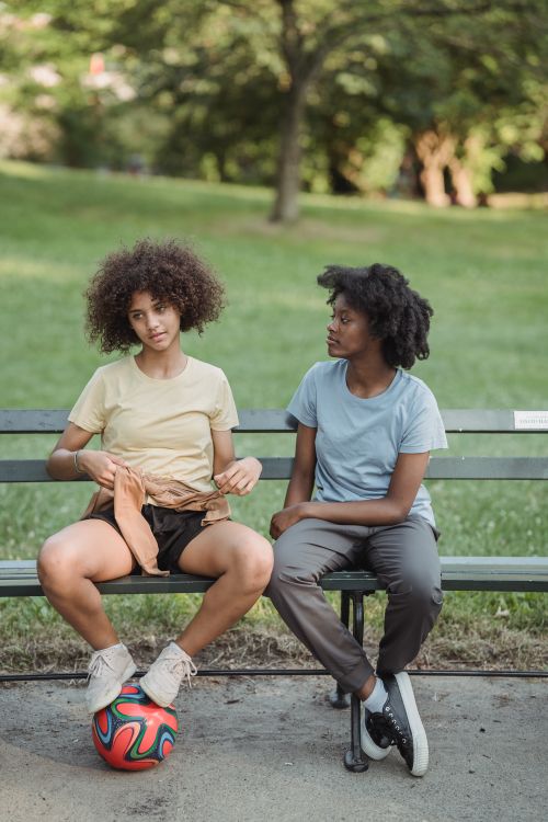 Free A mother and child sitting together on a bench in a sunny park with a colorful soccer ball. Stock Photo