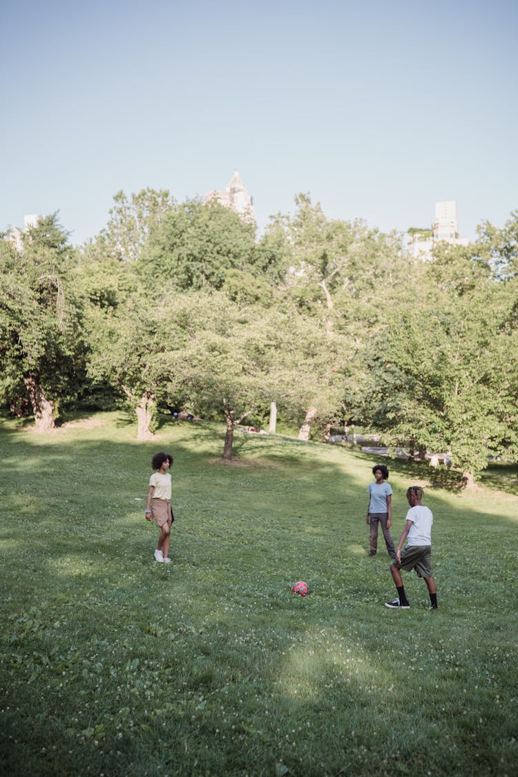 Three Teenagers Playing Football In The Park 