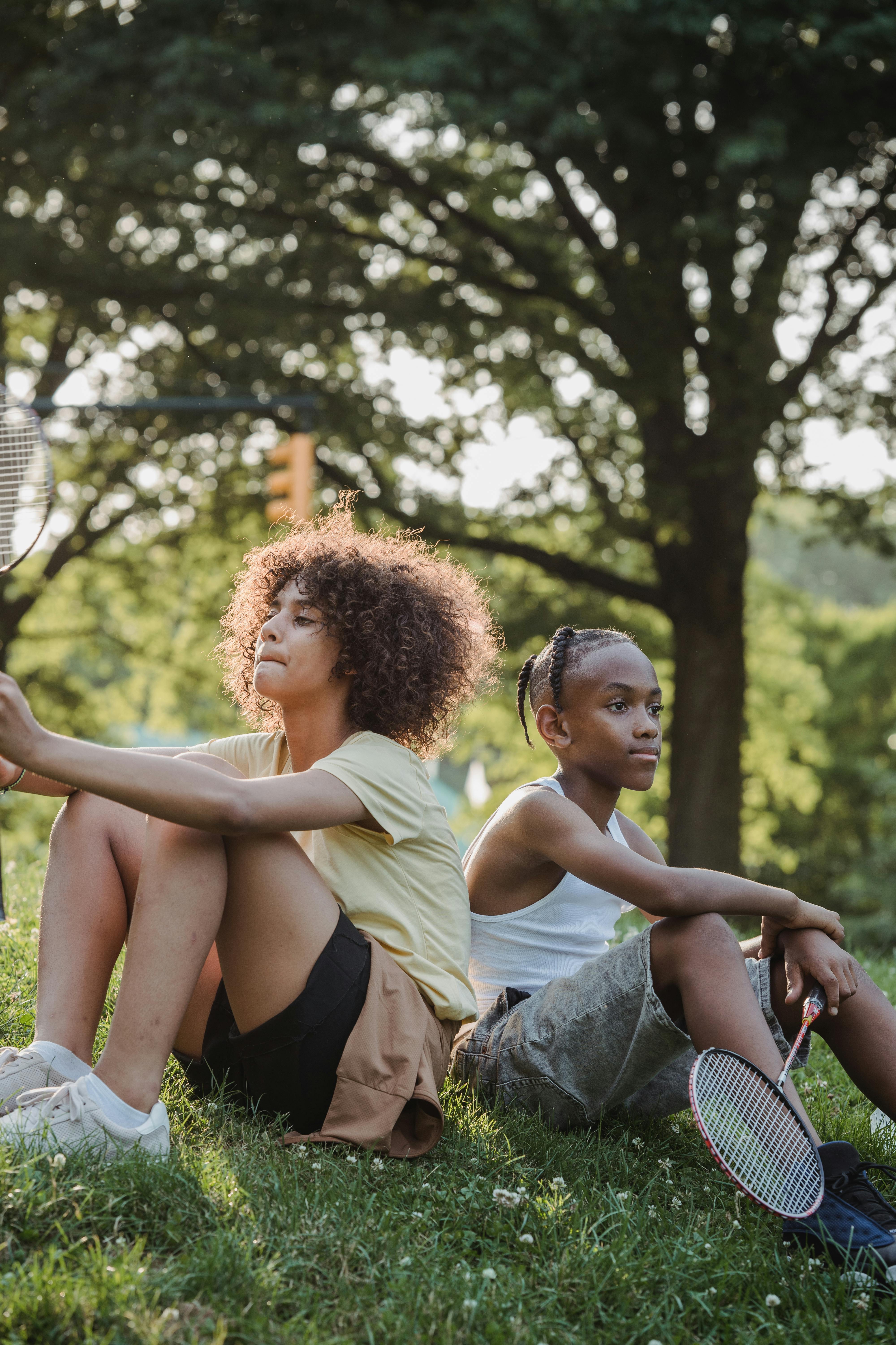 teenage girl sitting on the lawn with a boy holding a badminton racket