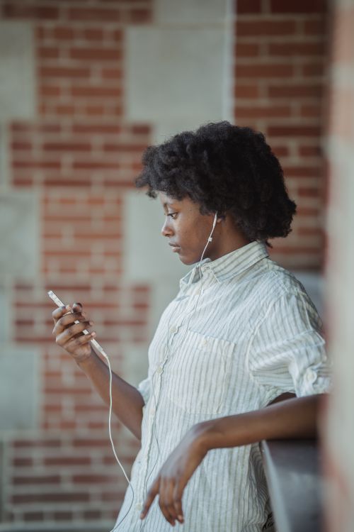 Free Side view of a woman listening to music with earphones outdoors against a brick wall. Stock Photo