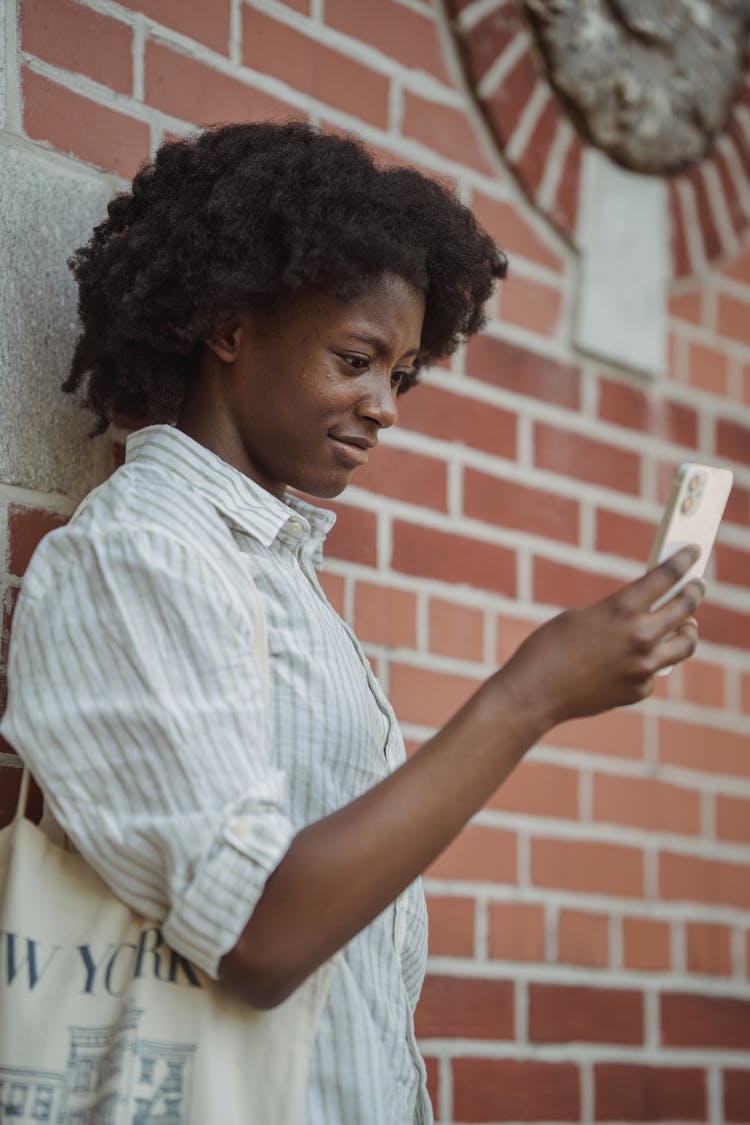 Woman Leaning Against A Wall Looking At Her Phone And Smiling 