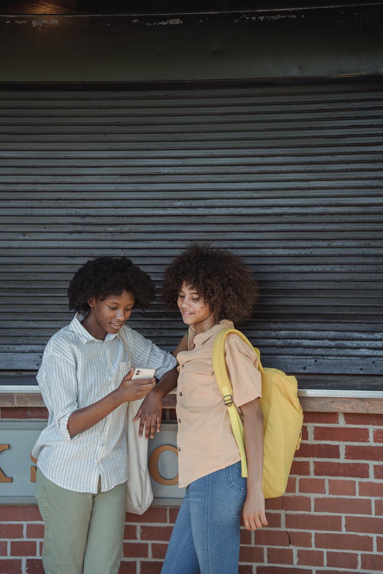 Women Leaning Against A Wall And Looking At Phone Screen