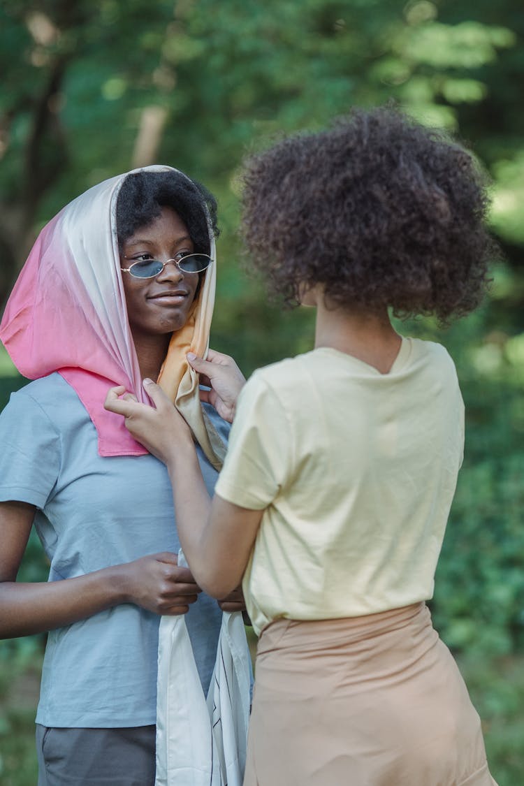 One Woman Putting A Headscarf On Another 