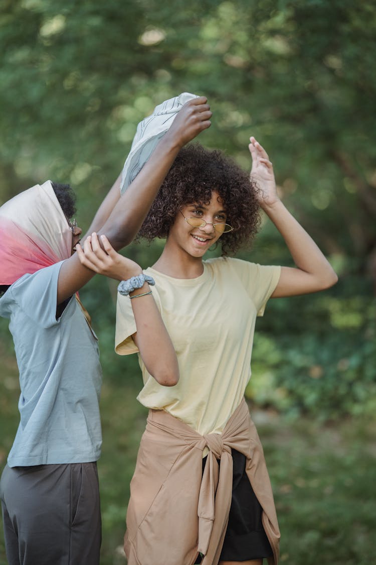 One Woman Putting A Headscarf On Another And Smiling 