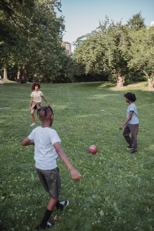 Free Three children playing football outdoors in a green park during a sunny summer day. Stock Photo
