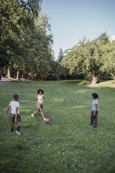 Three children enjoy a game of soccer on a sunny day in a lush park setting.