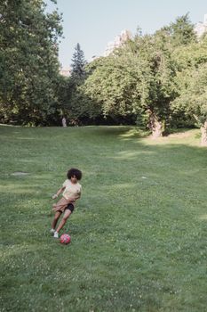 A playful child kicks a soccer ball on a sunny day in a lush green park, enjoying outdoor fun.