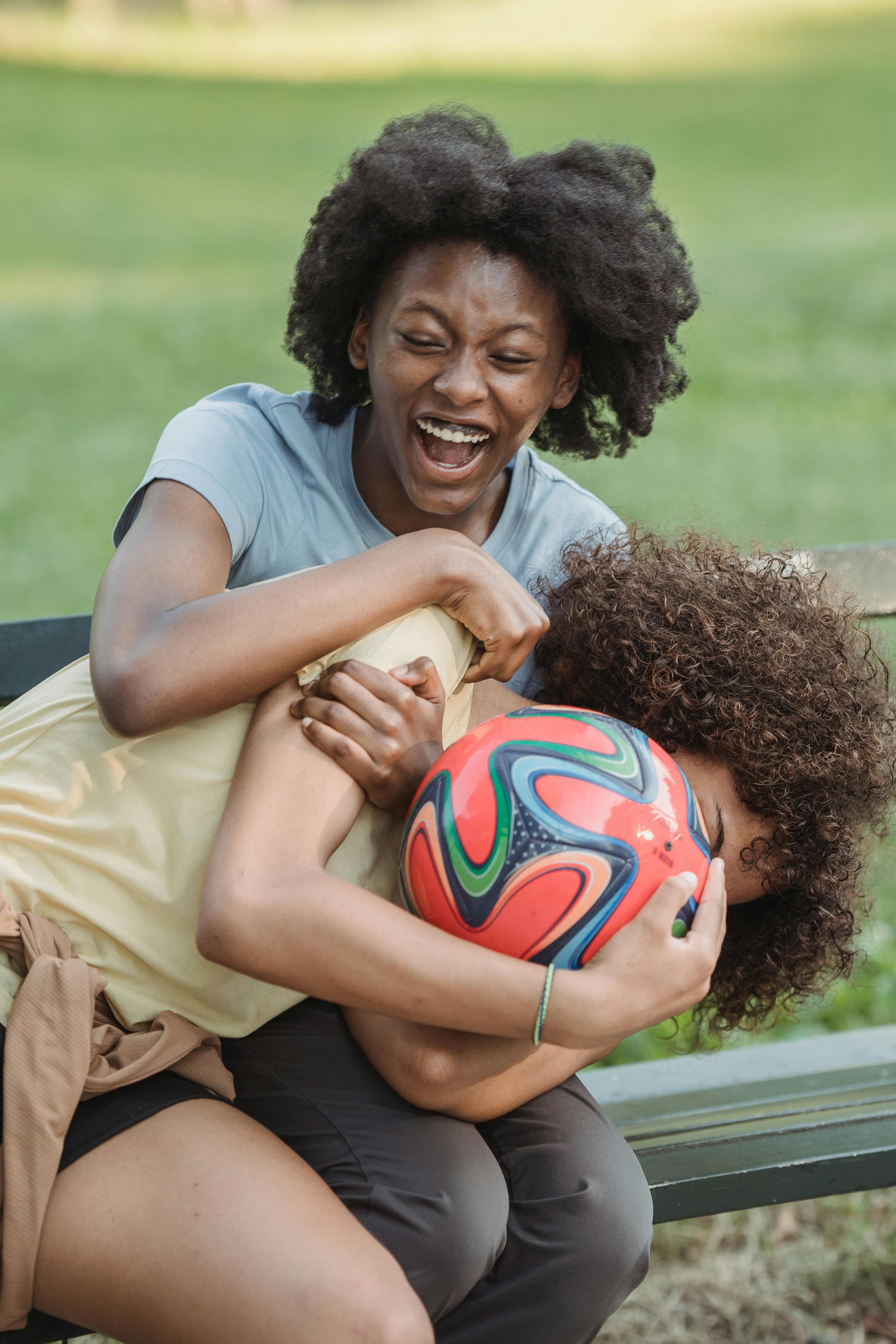 two young women play fighting for a football ball