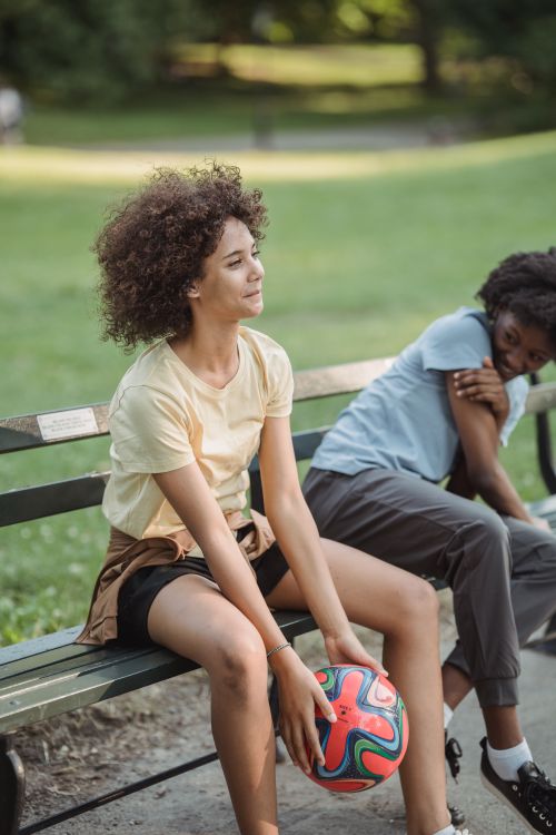 Free Two young women relaxing on a park bench with a colorful ball, enjoying summer leisure. Stock Photo