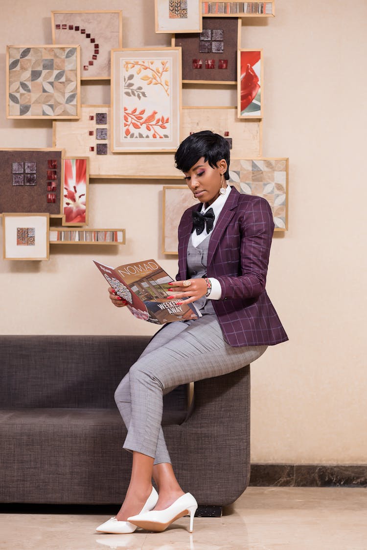 Woman In Suit Sitting On Couch Armrest Reading Magazine