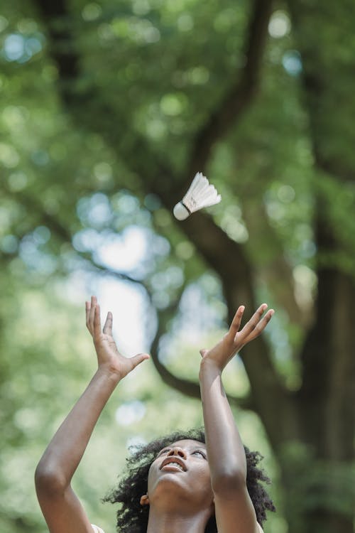Vertical Shot of a Girl Playing with a Badminton Shuttlecock and Trees in Background