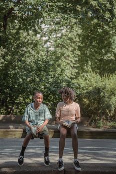 Two children sitting on a bench in a sunny park, engaged in reading books.
