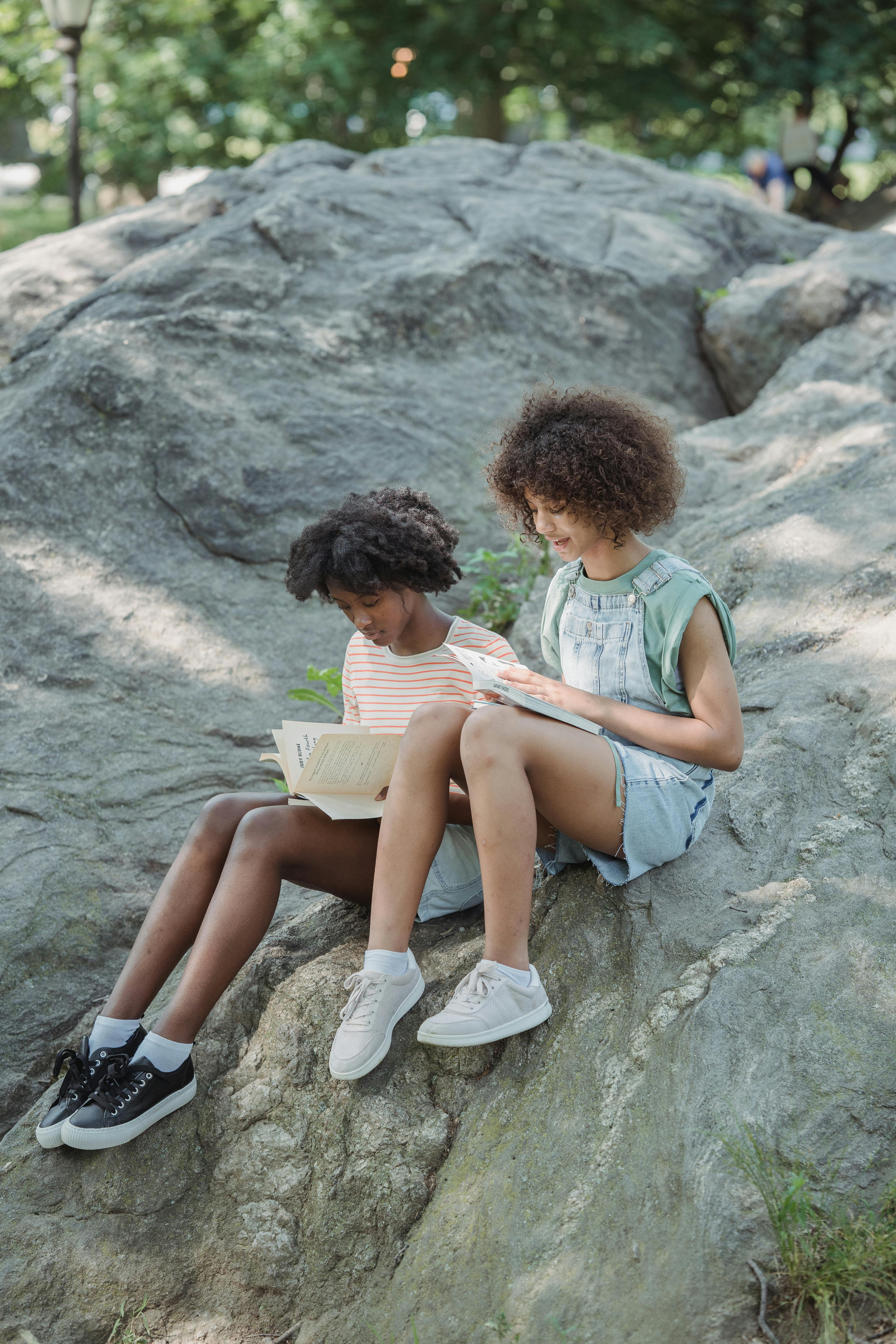 two young women sitting on a big rock and looking through their notebooks