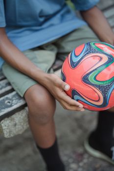 Close-up of a child holding a vibrant soccer ball while sitting on a bench, capturing a relaxed outdoor moment.
