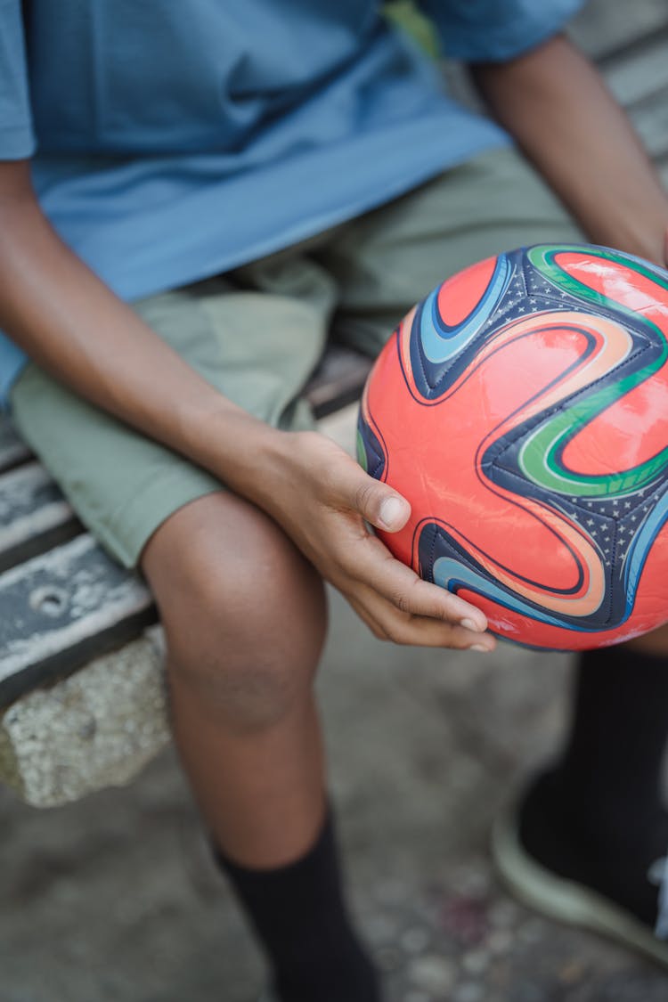 Close Up Of A Boy Sitting On A Bench And Holding A Red Ball