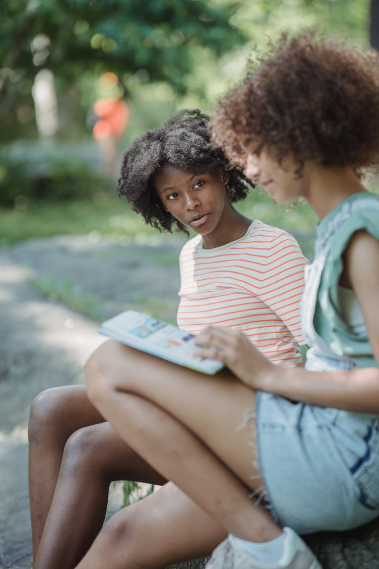 Portrait Of Girls Sitting With A Book In Park And Talking