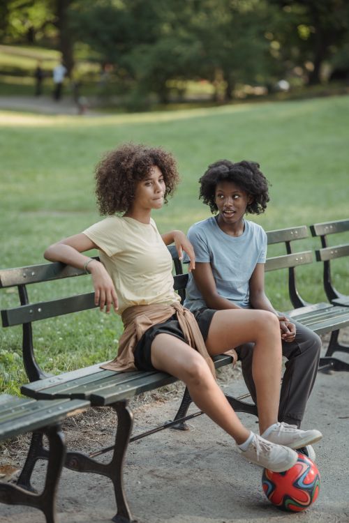 Free Two teenage girls sitting on a park bench, enjoying a warm day outdoors. Stock Photo