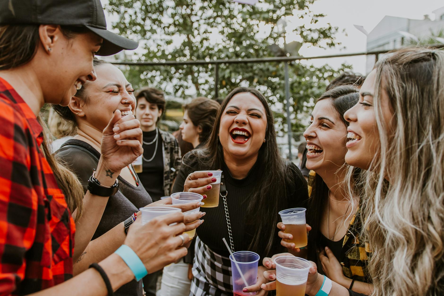 Group of young women laughing and enjoying drinks outdoors in São Paulo.