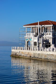 Elegant seaside building with scaffoldings, bordered by calm sea on a clear day.