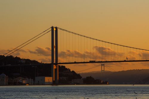 Free A scenic view of Istanbul's Bosphorus Bridge silhouetted against a golden sunset with calm waters. Stock Photo