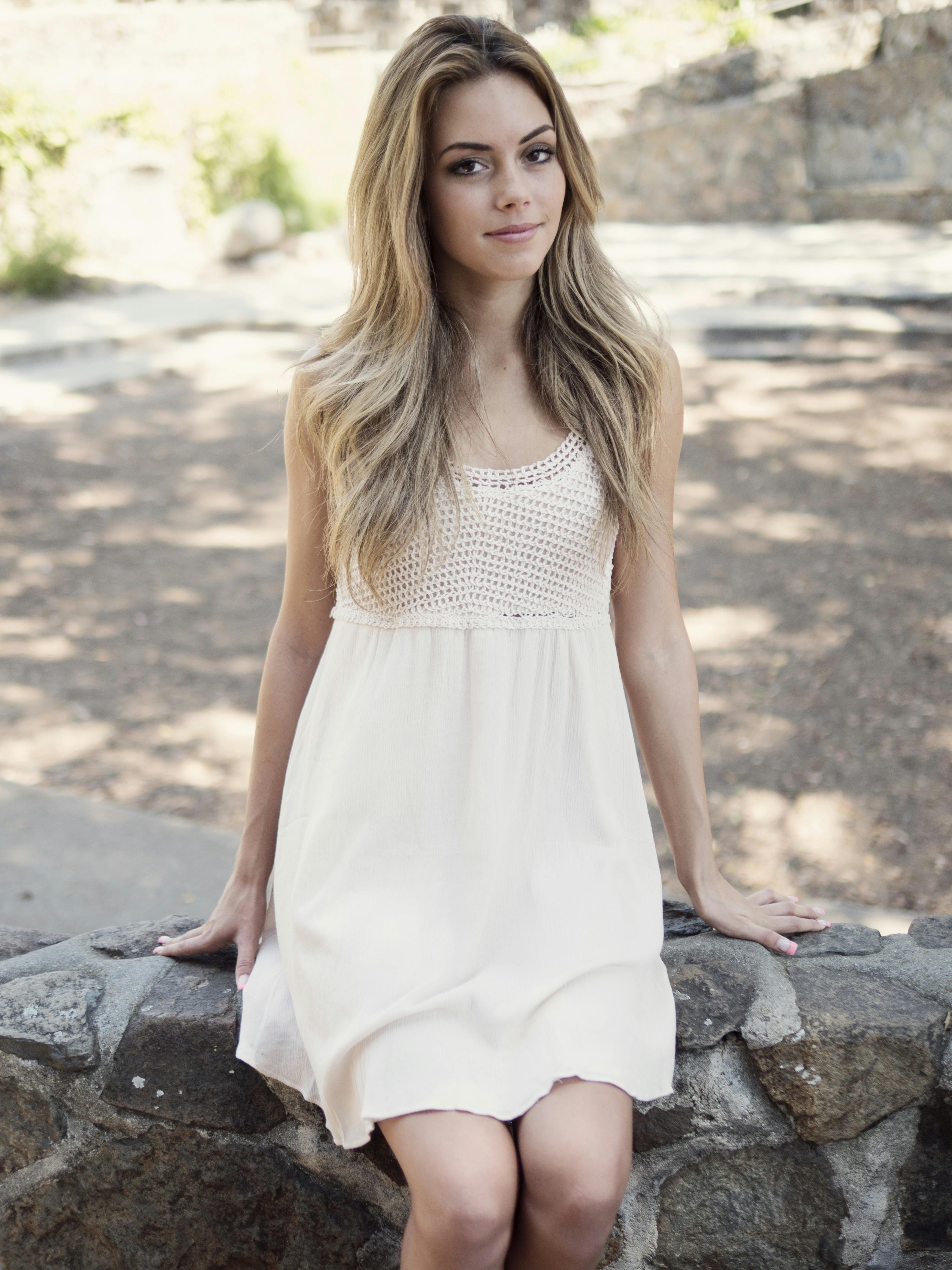 woman in white sleeveless dress sitting on gray concrete seat during daytime