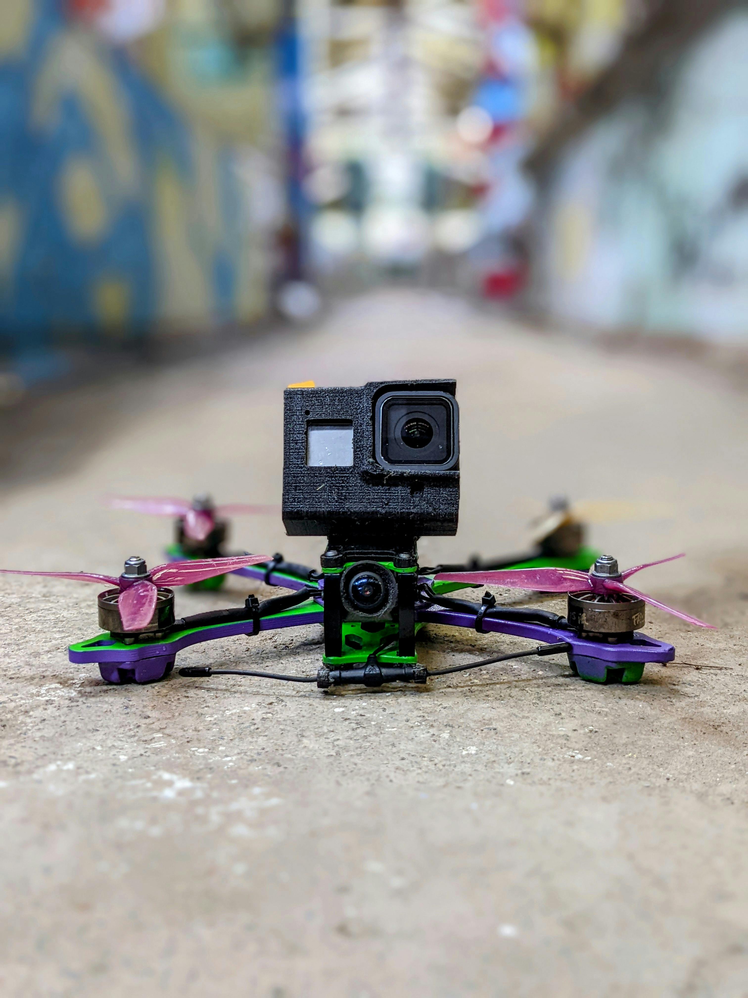 A close-up view of a drone equipped with an action camera, placed on a concrete surface in an urban setting.
