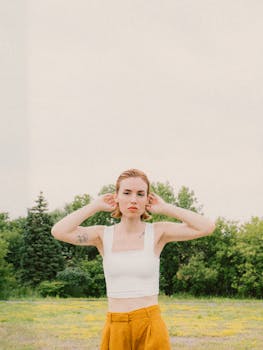 Portrait of a young woman in a white tank top outdoors against lush greenery.