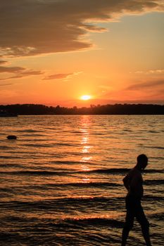 A serene sunset scene with a silhouette of a man walking by the beach, creating a peaceful vibe.