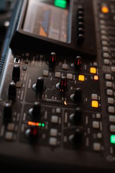 Detailed view of audio mixing console with illuminated controls and digital screen.