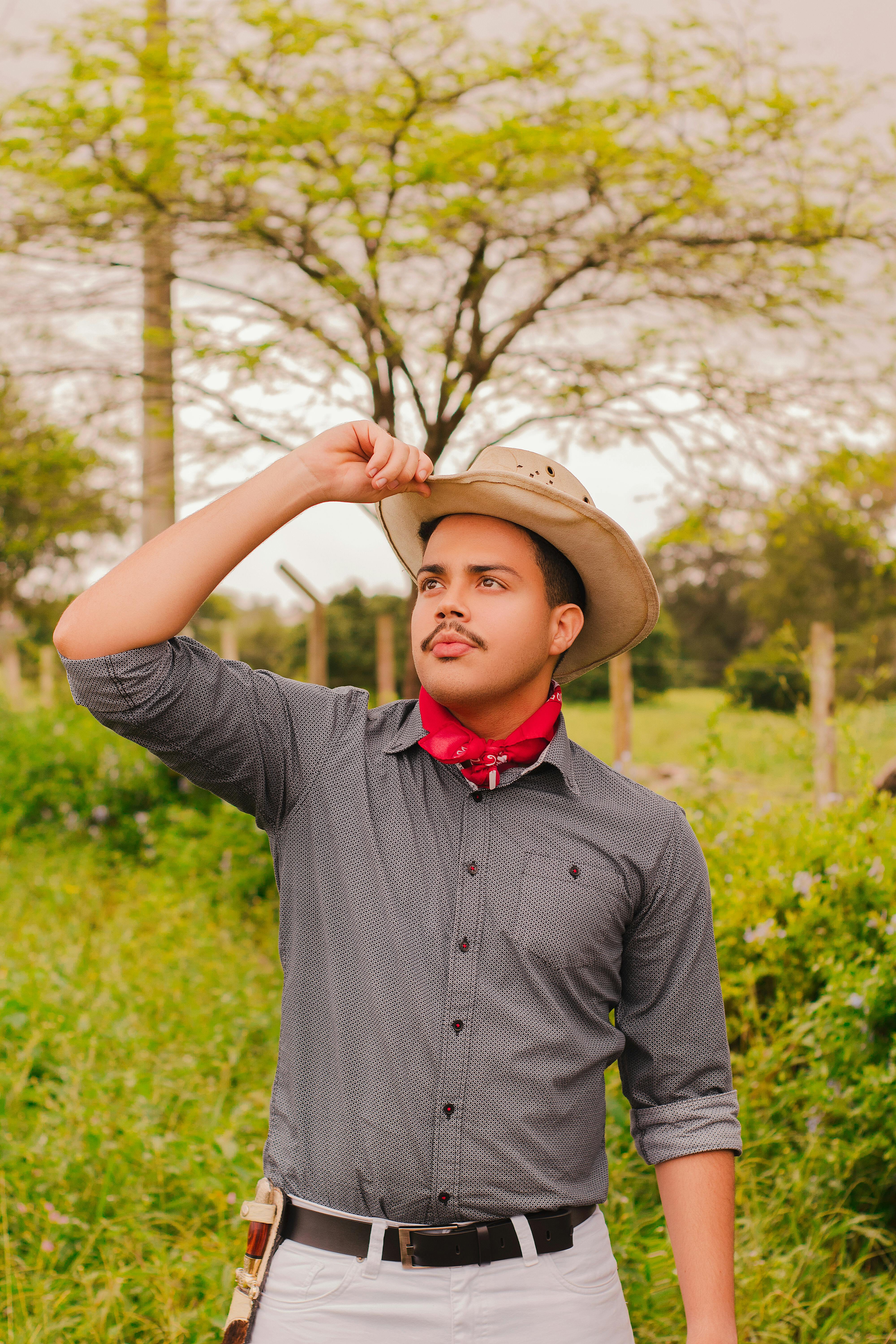 Portrait of a young man wearing a cowboy hat and red bandana in an outdoor farm setting.