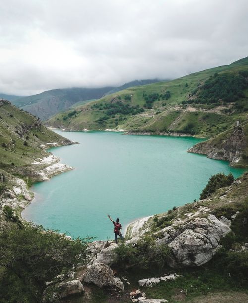 Free A person enjoying a stunning view of a turquoise mountain lake surrounded by lush hills. Stock Photo