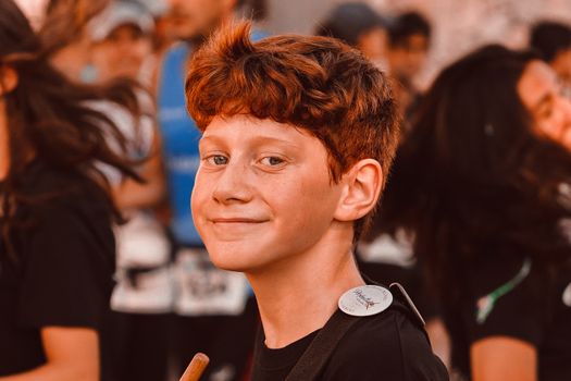 A young red-haired teen enjoying a lively outdoor event as part of a drum line.