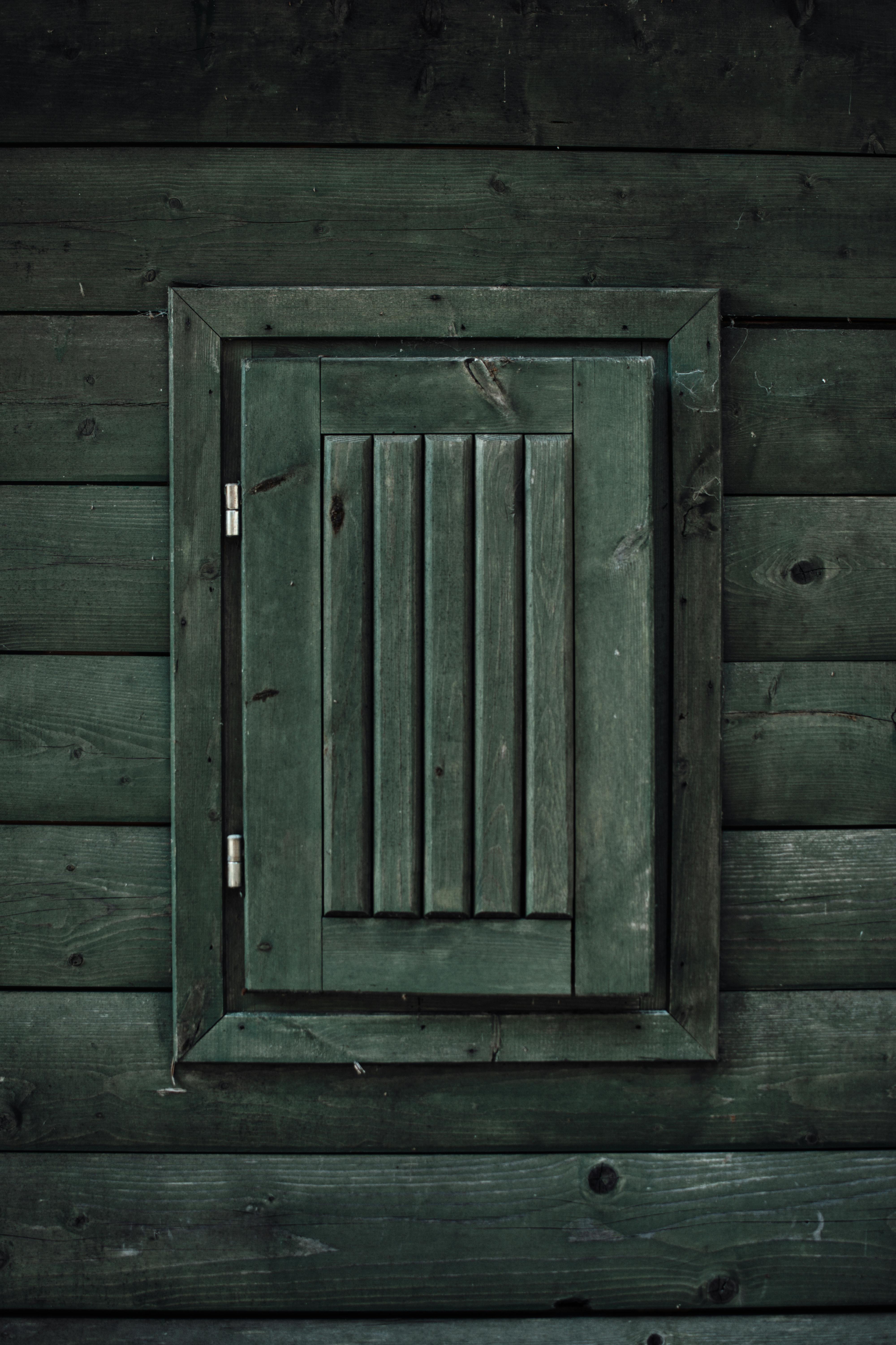 Vertical shot of an aged wooden window on a rustic dark wooden wall with rich texture.